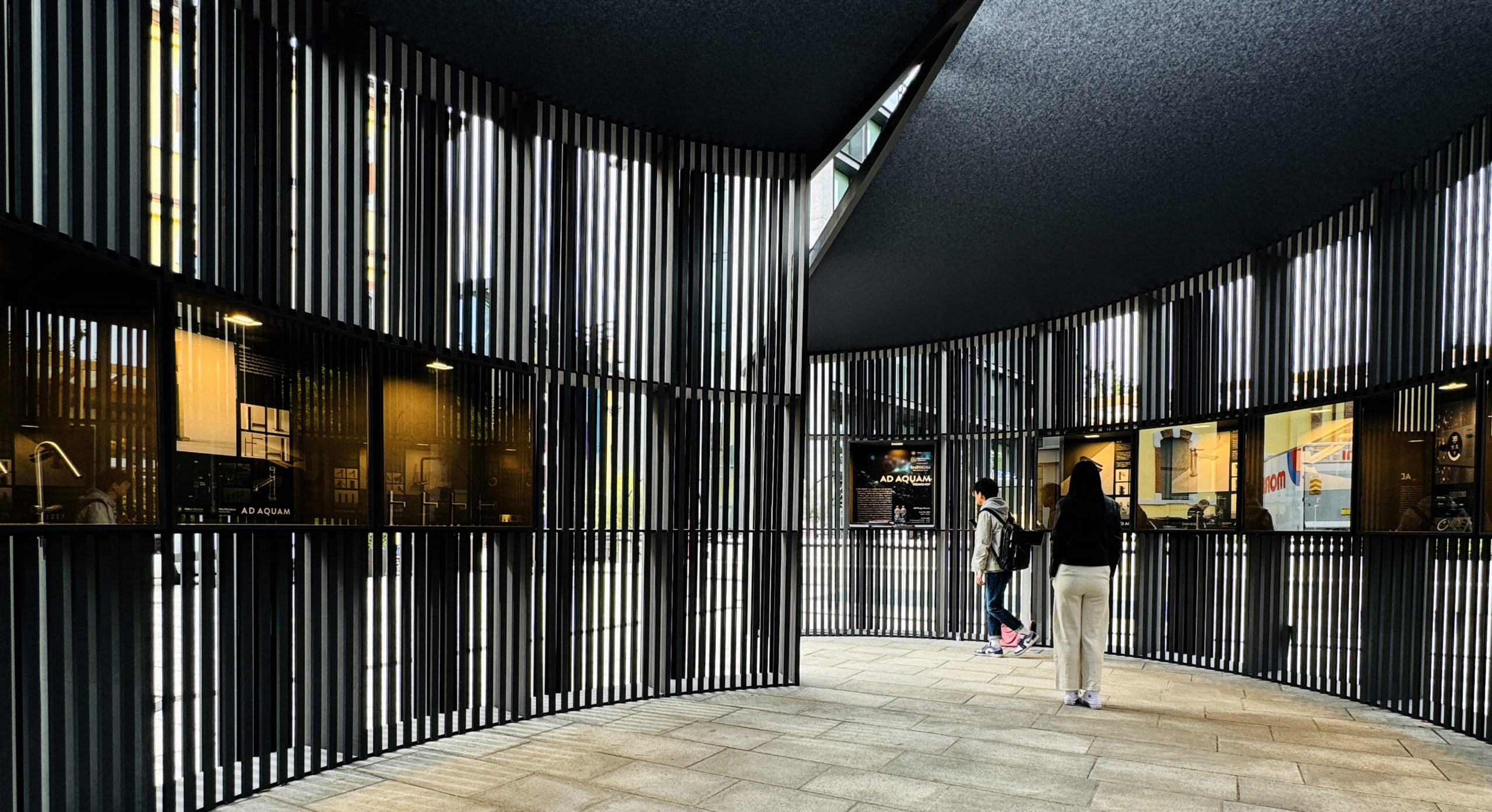 Visitors inside the AD AQUAM pavilion, surrounded by illuminated displays of student tap and shower-control concepts.